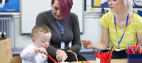 Nursery,Teacher,Sitting,With,A,Parent,And,Her,Down,Syndrome